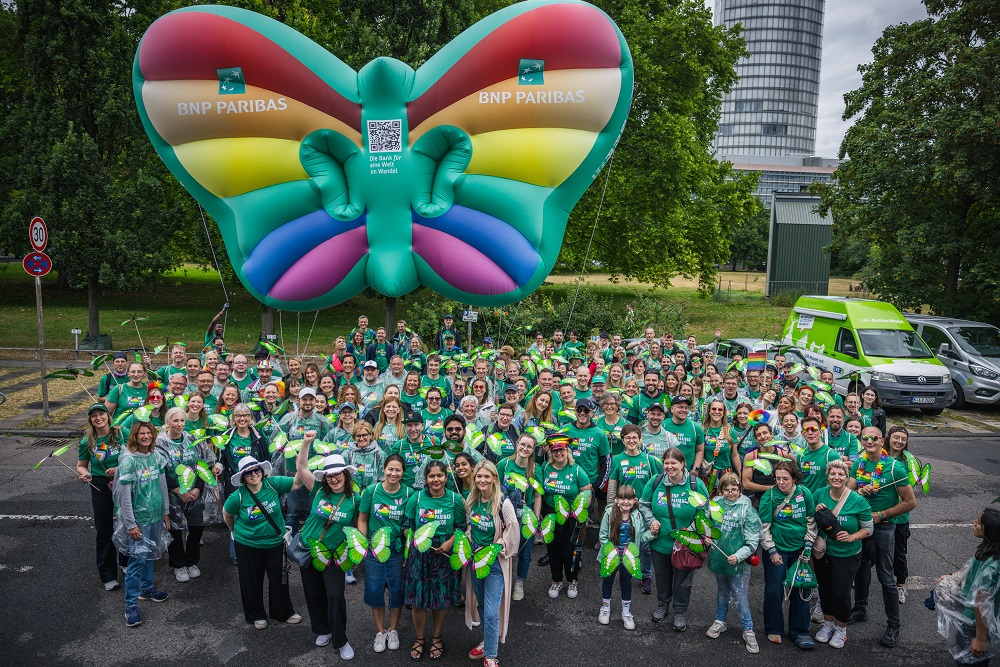 Große Gruppe von Menschen in grüner Kleidung vor einem aufblasbaren Schmetterling mit BNP Paribas-Logo beim CSD 2025